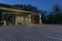 the front of a public building lit up at night with lights on, and sign saying presentation gallery