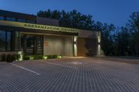 the front of a public building lit up at night with lights on, and sign saying presentation gallery