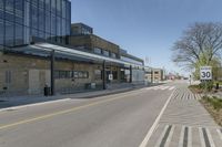 an empty street and sidewalk lined with brick walls, in front of a large building