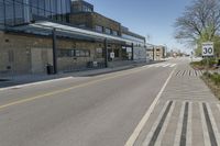 an empty street and sidewalk lined with brick walls, in front of a large building