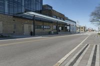 an empty street and sidewalk lined with brick walls, in front of a large building