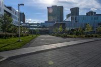 a city street surrounded by grass and tall buildings at the end of a street there is a paved pathway in front of the building