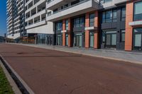 the empty road runs between a row of buildings near a grassy area near a brick sidewalk