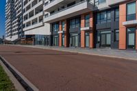 the empty road runs between a row of buildings near a grassy area near a brick sidewalk