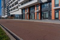 the empty road runs between a row of buildings near a grassy area near a brick sidewalk