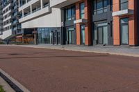 the empty road runs between a row of buildings near a grassy area near a brick sidewalk