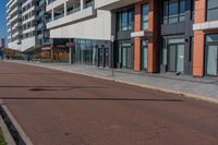 the empty road runs between a row of buildings near a grassy area near a brick sidewalk