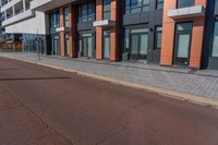 the empty road runs between a row of buildings near a grassy area near a brick sidewalk