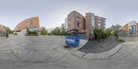 a distorted fish - eye photo shows a road and a big building with a blue dumpster in the middle