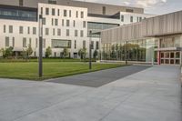 a city street surrounded by grass and tall buildings at the end of a street there is a paved pathway in front of the building