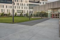 a city street surrounded by grass and tall buildings at the end of a street there is a paved pathway in front of the building