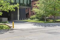 a street corner with a building, trees and bench in the foreground and a tree in front of it