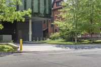 a street corner with a building, trees and bench in the foreground and a tree in front of it