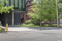 a street corner with a building, trees and bench in the foreground and a tree in front of it