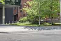 a street corner with a building, trees and bench in the foreground and a tree in front of it