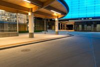 an empty road has a long walkway on it and buildings in the background with a light shine on