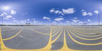 an empty parking lot with a number of yellow lines painted on it and a partly cloudy blue sky in the background