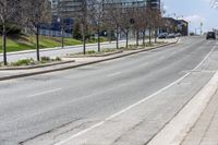 a road with a curb and parked cars on the side of it and buildings on the other side