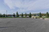 a large open parking lot with lots of buildings in the background and trees and grass