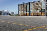 a parking lot in front of a glassed building with wooden slats on the outside