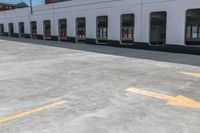 yellow arrows in an empty parking lot by an industrial building with large windows and signs