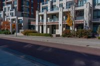 the apartment building next to the sidewalk has many windows on each of them and several trees