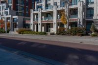 the apartment building next to the sidewalk has many windows on each of them and several trees