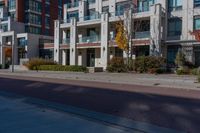 the apartment building next to the sidewalk has many windows on each of them and several trees