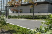 a motorcycle rider is riding on the street next to some trees and bushes with a glass building in the background