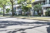 an empty street lined with trees next to a building in the middle of the day