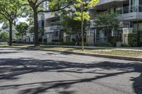 an empty street lined with trees next to a building in the middle of the day