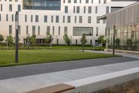 the bench is on the walkway in front of the building where there is a lawn and sidewalk