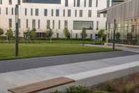 the bench is on the walkway in front of the building where there is a lawn and sidewalk