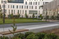 the bench is on the walkway in front of the building where there is a lawn and sidewalk