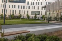 the bench is on the walkway in front of the building where there is a lawn and sidewalk