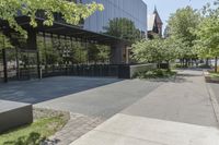 the sidewalk leading to an office building and sidewalk with bushes on either side and trees in the background