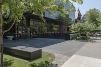 the sidewalk leading to an office building and sidewalk with bushes on either side and trees in the background