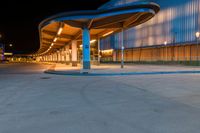 the empty sidewalk at a bus station in the city at night time with light on