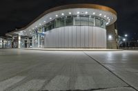 an empty parking lot at night with many windows at its side and lights on the windows