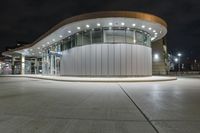 an empty parking lot at night with many windows at its side and lights on the windows