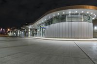 an empty parking lot at night with many windows at its side and lights on the windows