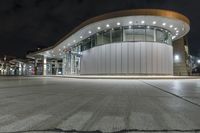 an empty parking lot at night with many windows at its side and lights on the windows