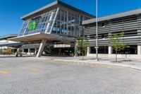 a grey building with a roof and glass windows that has a green sign in the front