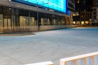 an empty sidewalk at night in front of a modern building with glass doors and a street light