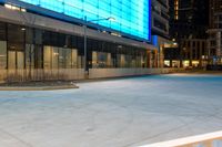 an empty sidewalk at night in front of a modern building with glass doors and a street light