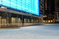 an empty sidewalk at night in front of a modern building with glass doors and a street light