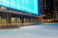 an empty sidewalk at night in front of a modern building with glass doors and a street light