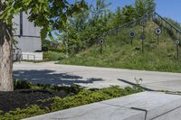 a green grassy hill and some trees on the side of a sidewalk near steps with arrows and signs in a circle