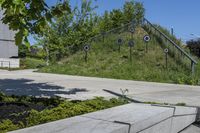 a green grassy hill and some trees on the side of a sidewalk near steps with arrows and signs in a circle