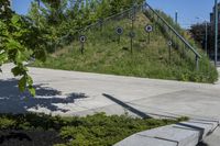 a green grassy hill and some trees on the side of a sidewalk near steps with arrows and signs in a circle